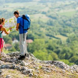 Couple of hikers reading a map on a rocky hilltop overlooking green valleys